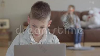 小男孩坐在笔记本电脑上，小女孩，他的孪生妹妹在家里的沙发上吹肥皂泡